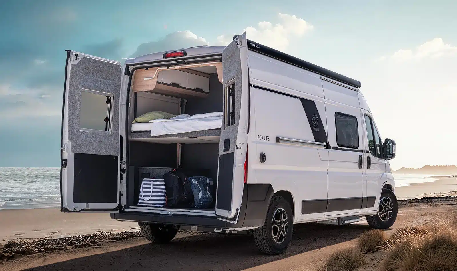 KNAUS BOXLIFE Camper Van mit geöffneten Hecktüren am Strand, Blick auf das flexible Heckbett und Gepäckraum