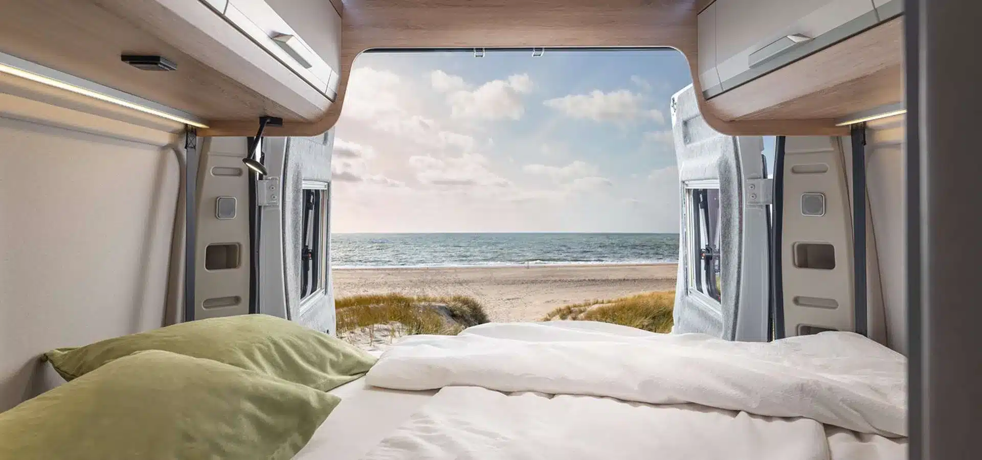 Blick vom Bett eines KNAUS BOXLIFE Camper Vans durch das geöffnete Heck auf einen Strand mit Meer