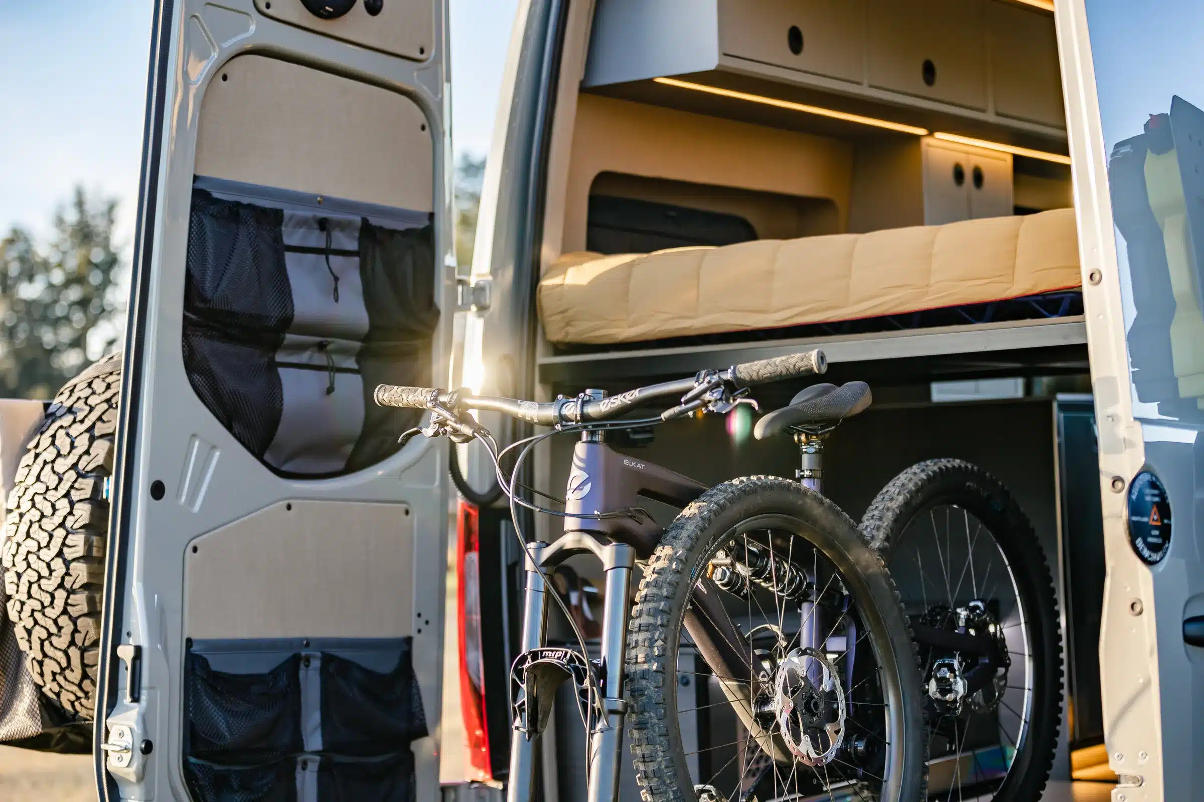 Blick in das geöffnete Heck eines ausgebauten Mercedes Sprinter Vans mit Plattformbett, Stauraum und Mountainbike