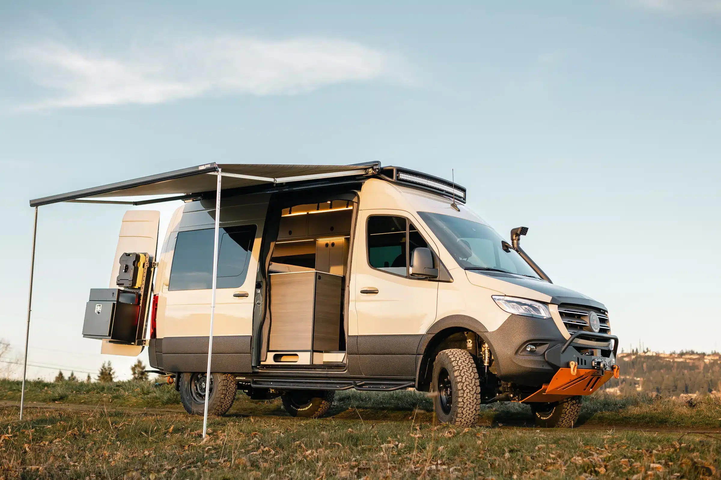 Mercedes Sprinter 144 4x4 Campervan mit ausgefahrener Markise und Offroad-Umbau auf einer Wiese
