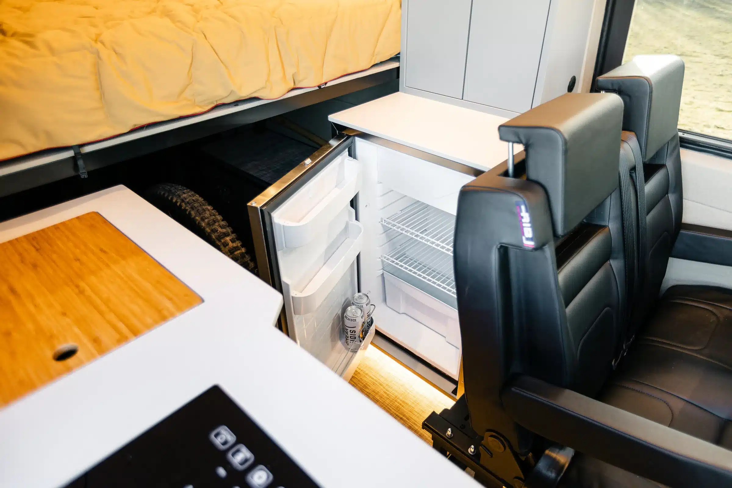 Offener Kühlschrank im Innenraum eines ausgebauten Mercedes Sprinter 4x4 Campervans mit Sitzbank und Bett