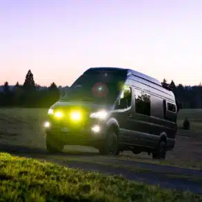 Mercedes Sprinter 170 4x4 Campervan Leithaus mit eingeschaltetem Licht auf einem Feldweg bei Sonnenuntergang
