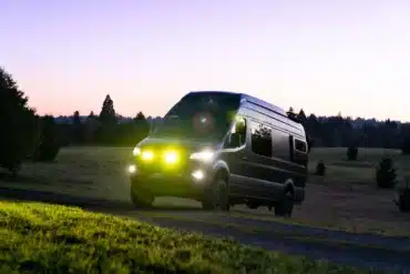 Mercedes Sprinter 170 4x4 Campervan Leithaus mit eingeschaltetem Licht auf einem Feldweg bei Sonnenuntergang