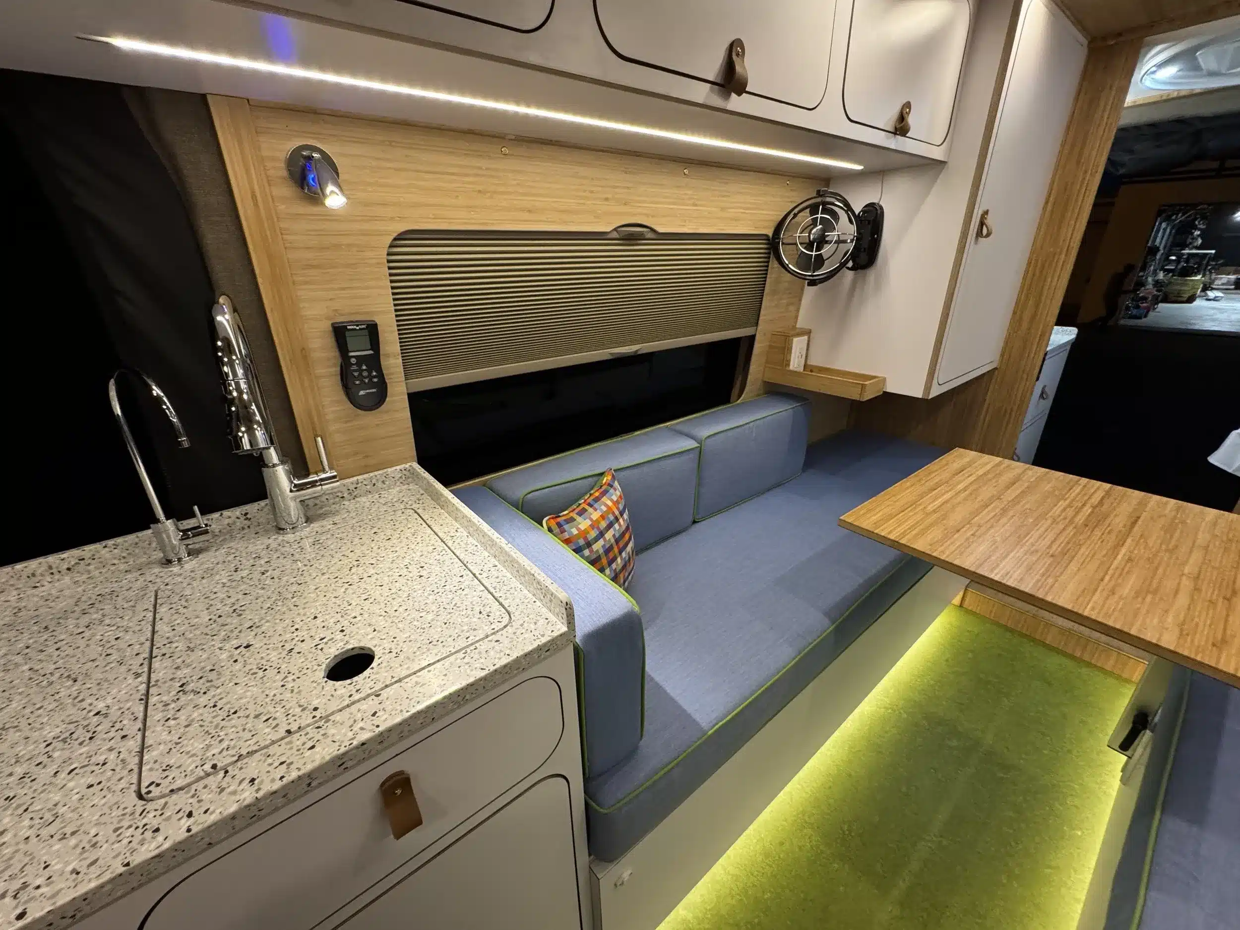 Innenansicht eines modernen Campervans mit Küchenzeile, Sitzbank, Tisch und Stauraum, hochwertige Materialien und LED-Beleuchtung