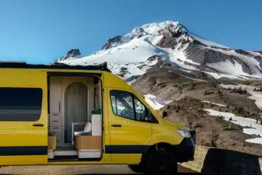 Gelber Luna Van mit offenem Schiebetür, Blick auf den stilvollen Innenraum, im Vordergrund eine Berglandschaft mit Schnee