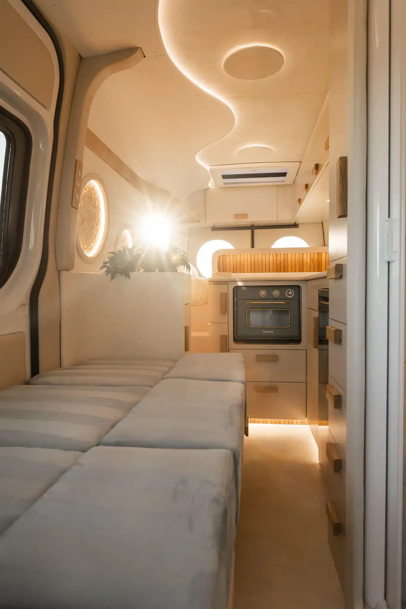 Innenraum des Luna Van von Rogue Vans mit L-förmiger Küche, modularer Sitz- und Schlaflösung, runden Fenstern und mediterran inspiriertem Design