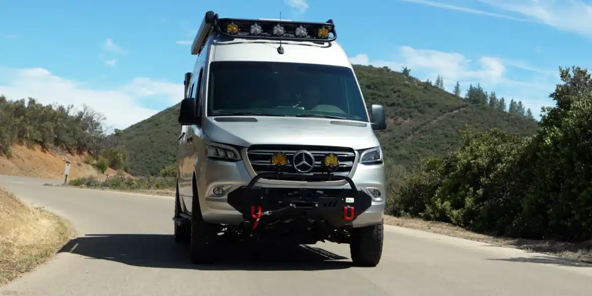 Frontansicht eines silbernen McCoy Palisade Campervans von Rogue Vans auf einer Landstraße, umgeben von Hügeln und Vegetation