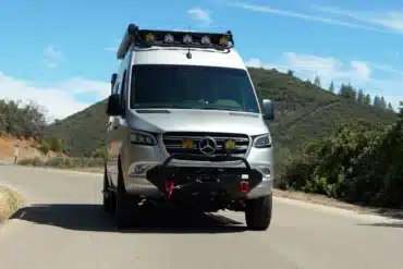Frontansicht eines silbernen McCoy Palisade Campervans von Rogue Vans auf einer Landstraße, umgeben von Hügeln und Vegetation