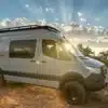 Mercedes Sprinter 4x4 Azure Campervan mit Dachträger und Offroad-Bereifung auf einer Wiese bei Sonnenuntergang