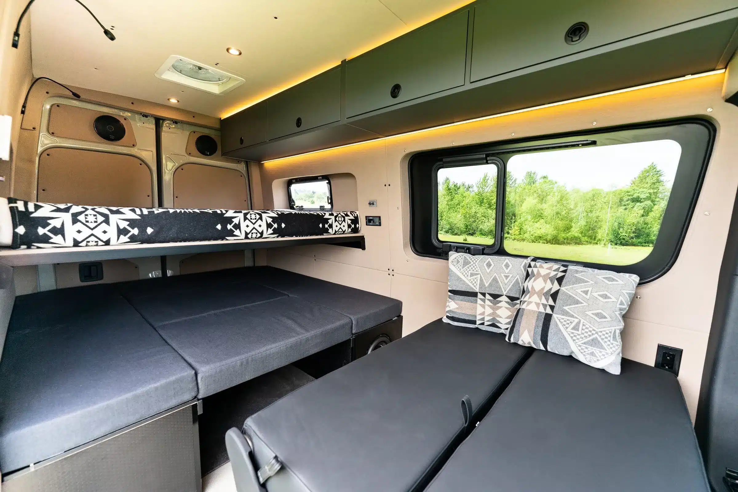 Innenansicht eines ausgebauten Mercedes Sprinter 144 High Roof mit Schlaf- und Sitzbereich, modernen Schränken und großen Fenstern