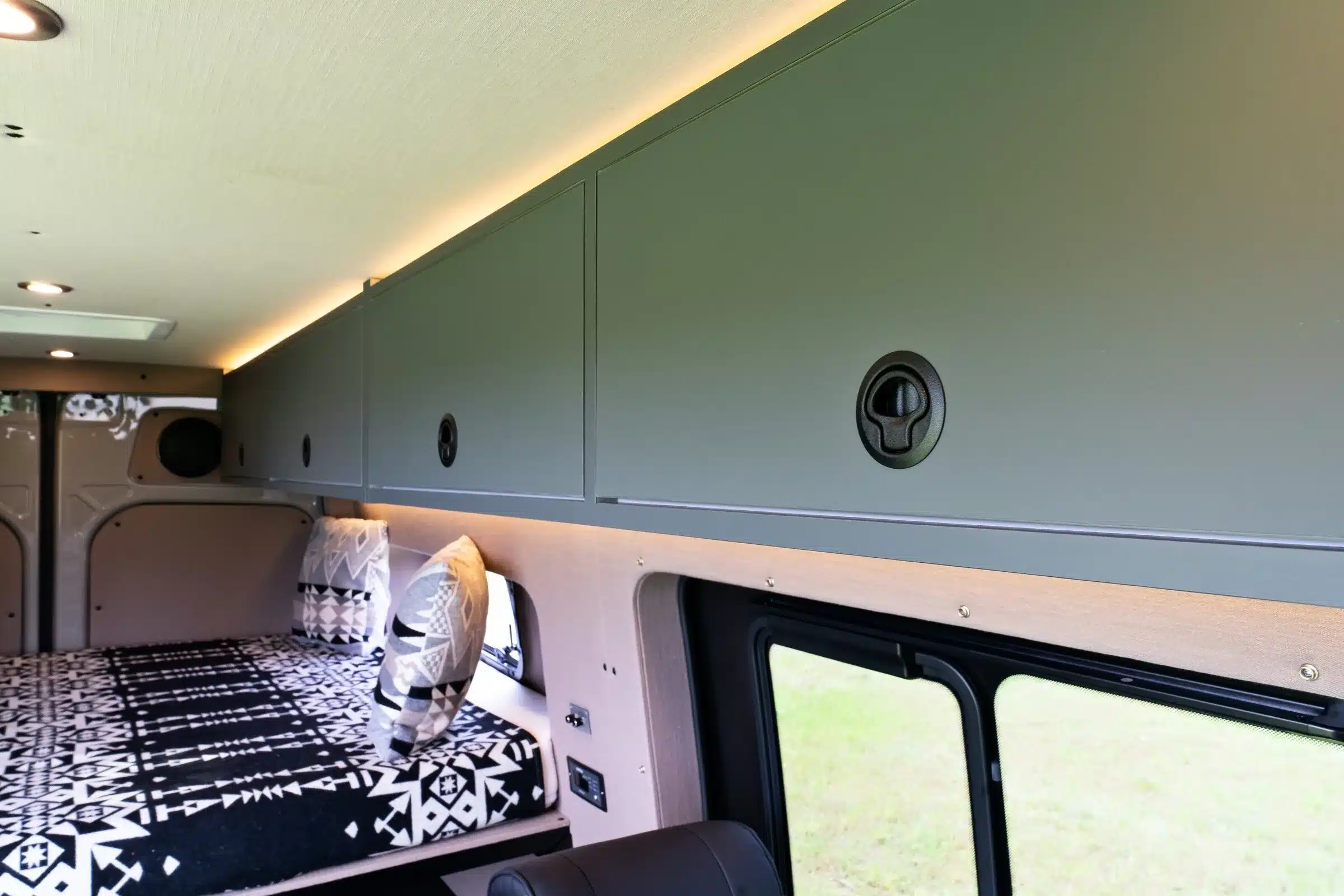 Innenansicht eines ausgebauten Mercedes Sprinter 144 High Roof mit modernen Hängeschränken, Bett und Kissen