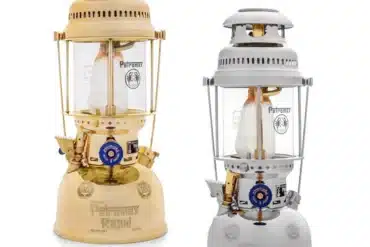 Zwei Petromax HK500 Petroleumlampen, eine in Messing, eine in Chrom, nebeneinander auf weißem Hintergrund