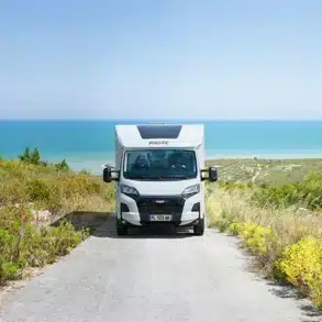 Pilote P620D Expression Wohnmobil fährt auf einer schmalen Straße mit Meerblick im Hintergrund