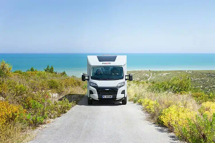 Pilote P620D Expression Wohnmobil fährt auf einer schmalen Straße mit Meerblick im Hintergrund