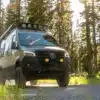 Mercedes Sprinter 144 AWD Quiet Flight Campervan mit Offroad-Ausstattung und Dachträger fährt auf Waldweg