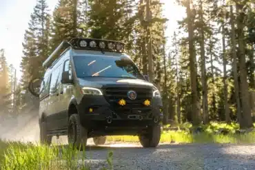 Mercedes Sprinter 144 AWD Quiet Flight Campervan mit Offroad-Ausstattung und Dachträger fährt auf Waldweg