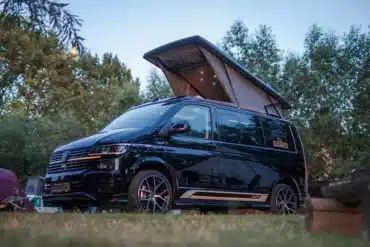 VW T6.1 Campervan Rhön Camp DER ULTIMATE mit geöffnetem Skyline Aufstelldach auf einem Campingplatz