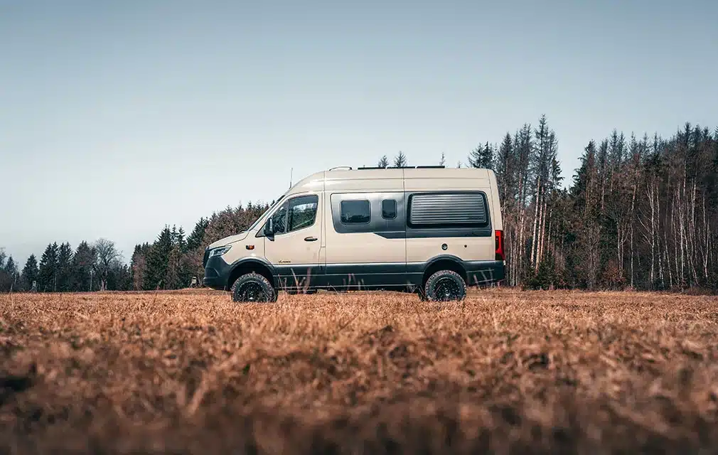 Rhön Camp THE FORCE Campervan auf Basis eines Mercedes Sprinter, stehend auf einer Wiese vor einem Wald