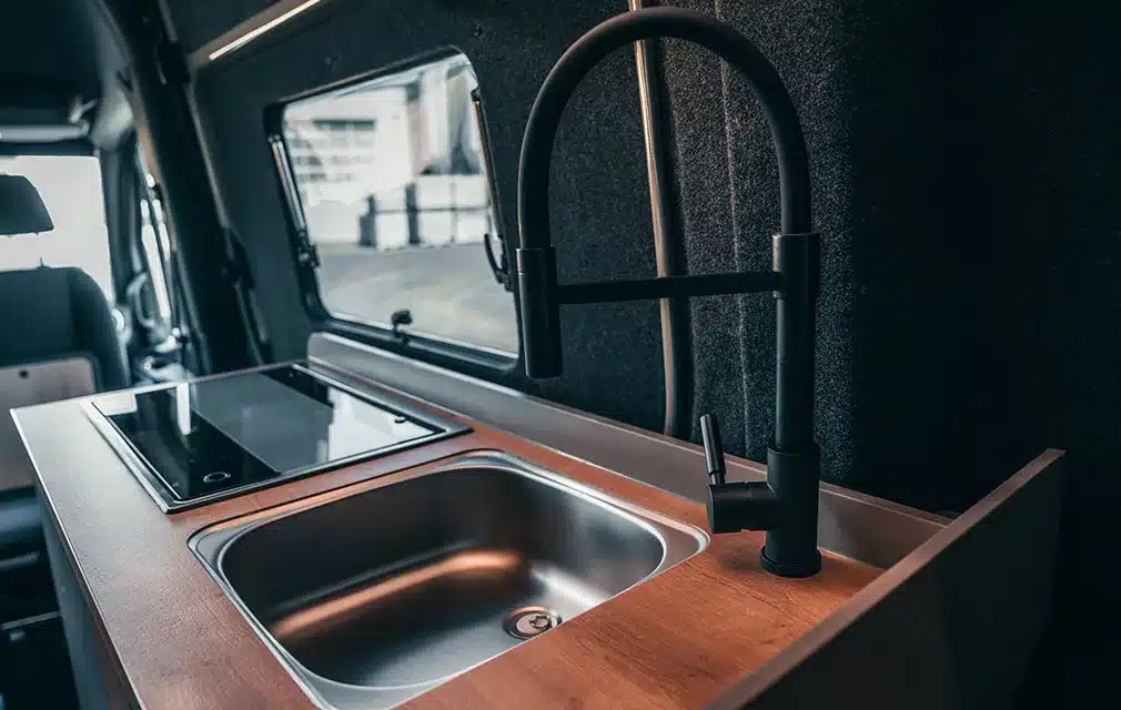 Detailansicht der Küchenzeile mit Spüle, Wasserhahn und Kochfeld im Rhön Camp THE FORCE Camper auf Mercedes Sprinter Basis
