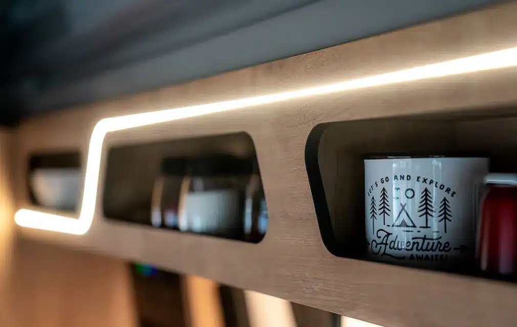 Nahaufnahme eines offenen Regals mit LED-Beleuchtung und Tassen im Innenraum des Rhön Camp The Pace Campers