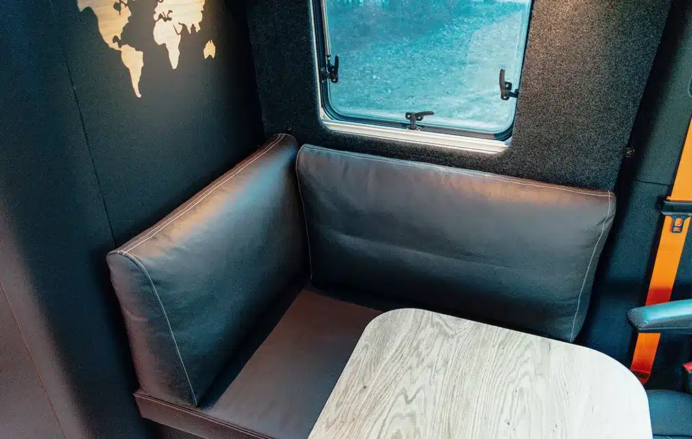 Leder-Sitzbank mit Holztisch und Fenster im Innenraum des Rhön Camp The Specter