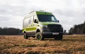 Grüner Rhön Camp THE SPIRIT Campervan auf Mercedes Sprinter Basis steht auf einer Wiese vor bewaldetem Hintergrund