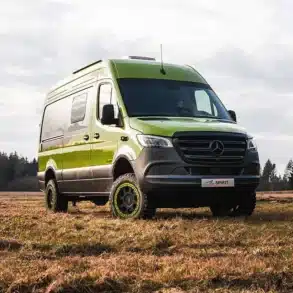 Grüner Rhön Camp THE SPIRIT Campervan auf Mercedes Sprinter Basis steht auf einer Wiese vor bewaldetem Hintergrund