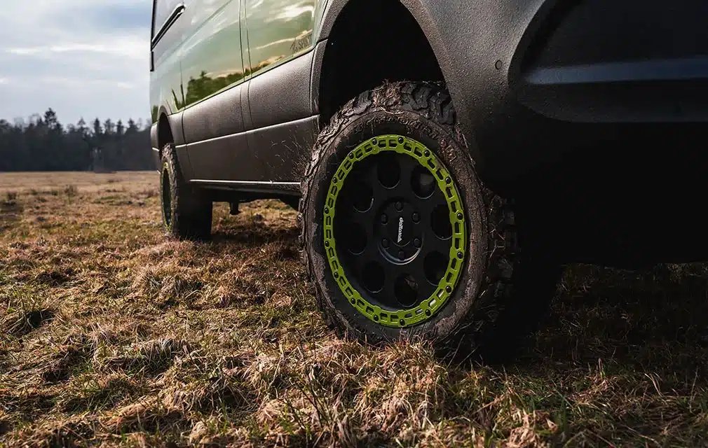 Nahaufnahme eines grobstolligen Offroad-Reifens mit grünem Felgenring an einem Rhön Camp THE SPIRIT auf einer Wiese