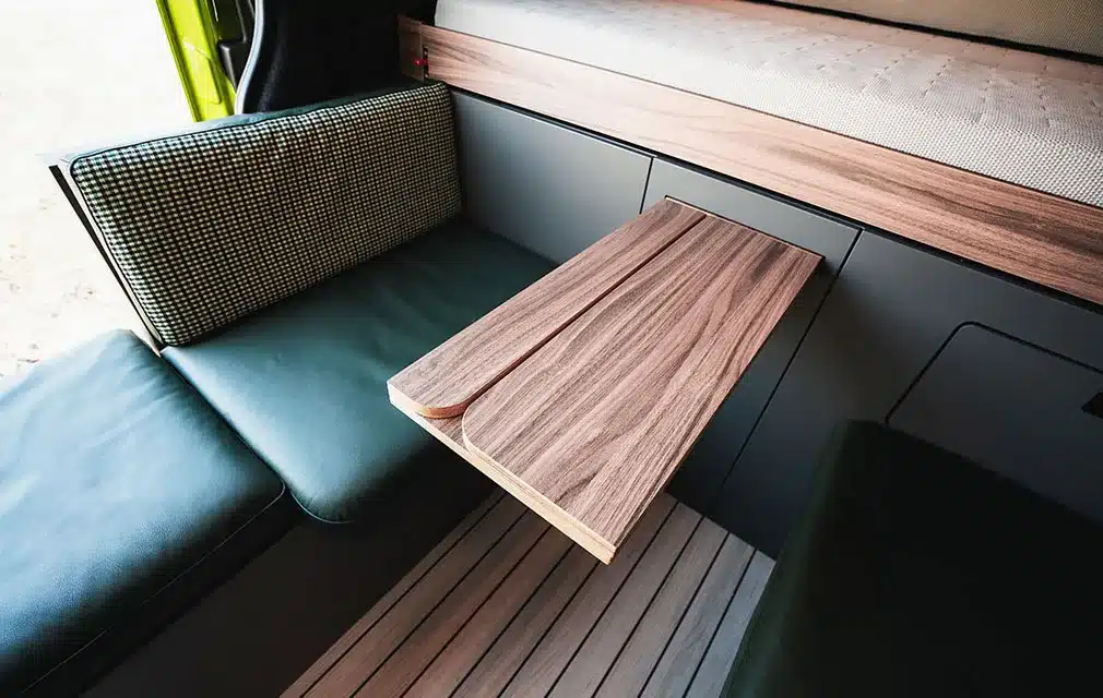Sitzbank mit grünem Polster und Klapptisch aus Holz im Innenraum des Rhön Camp THE SPIRIT Campervans