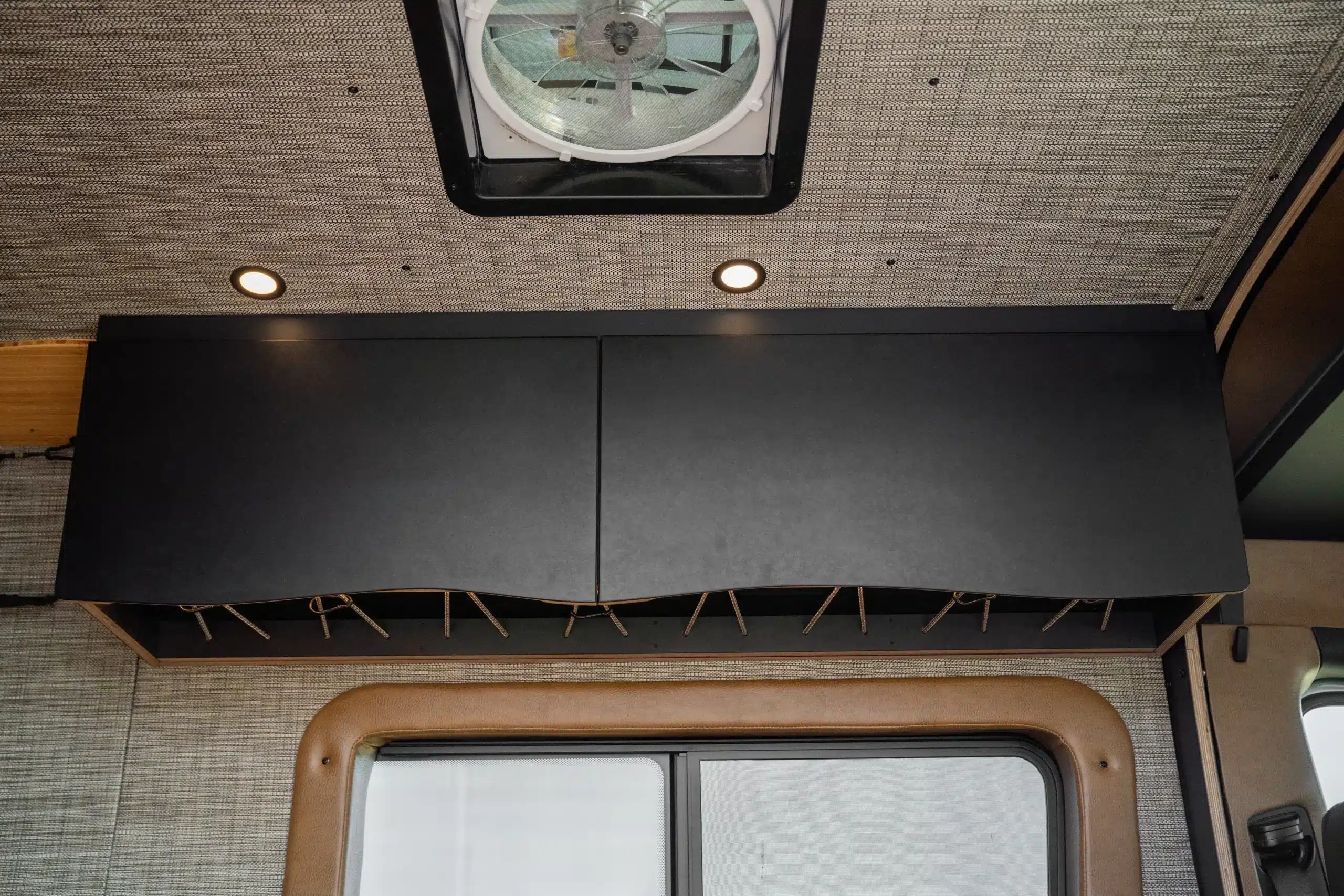 Schwarzer Oberschrank mit wellenförmiger Unterkante und Seilaufhängung im Innenraum eines ausgebauten Vans