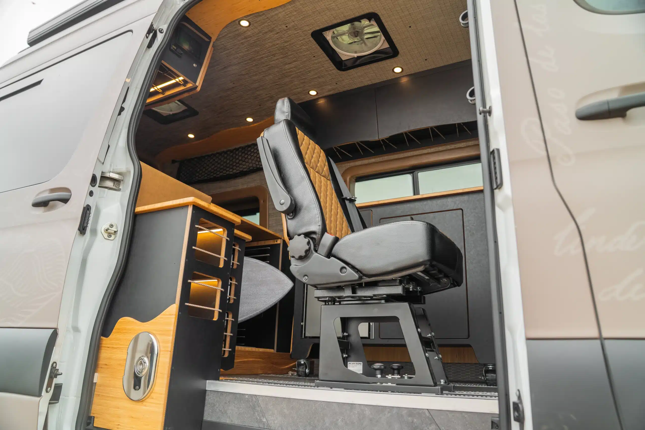 Blick in den Innenraum eines ausgebauten Surf-Vans mit drehbarem Einzelsitz, Bambus-Arbeitsflächen und moderner Ausstattung