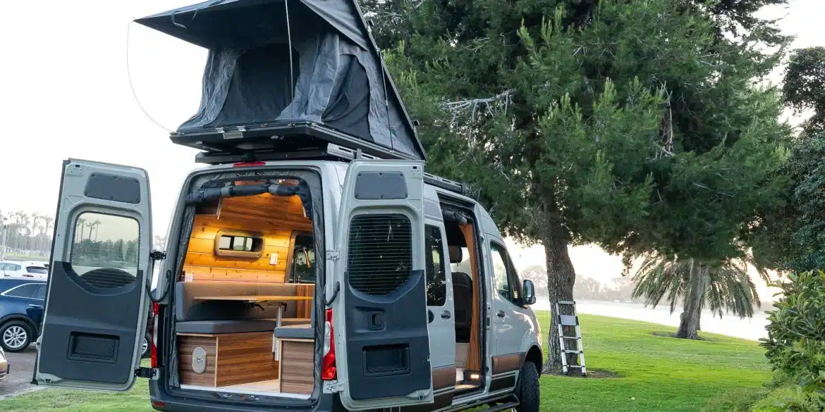 Heckansicht eines hochwertigen Campervans mit geöffnetem Dachzelt und modernem Innenausbau, geparkt auf einer Wiese
