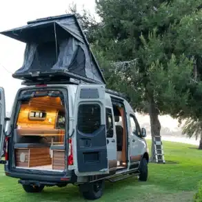 Heckansicht eines hochwertigen Campervans mit geöffnetem Dachzelt und modernem Innenausbau, geparkt auf einer Wiese