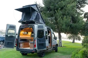 Heckansicht eines hochwertigen Campervans mit geöffnetem Dachzelt und modernem Innenausbau, geparkt auf einer Wiese