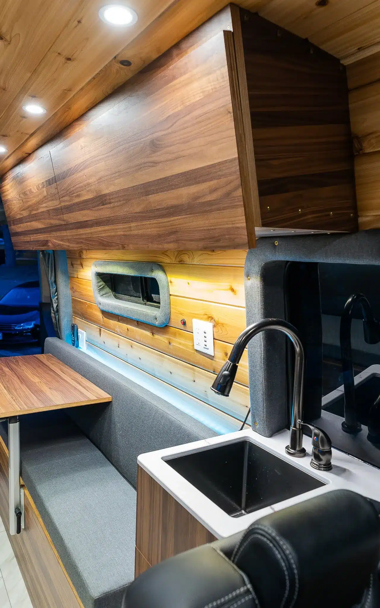 Moderne Küchenzeile und Sitzgruppe im Innenraum eines ausgebauten Vans mit Holzverkleidung und LED-Beleuchtung