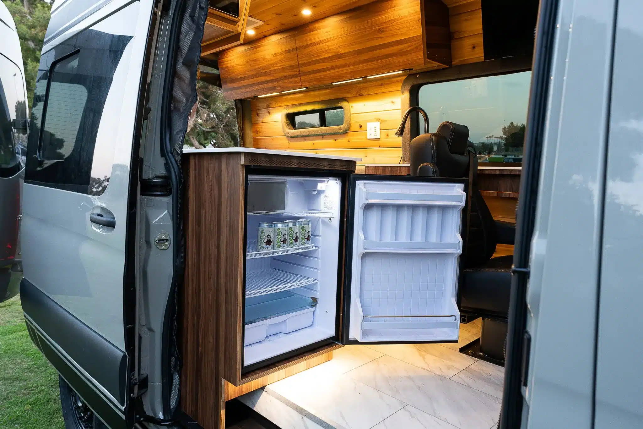 Geöffneter Kühlschrank in einer modernen Küchenzeile mit Holzverkleidung im Innenraum eines ausgebauten Vans