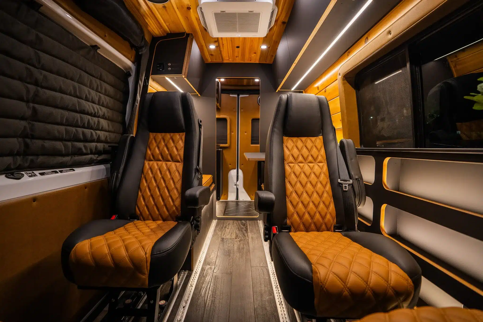 Innenansicht des Rogue Stratos Campervan mit zwei lederbezogenen Kapitänsstühlen, Holzdecke und moderner LED-Beleuchtung
