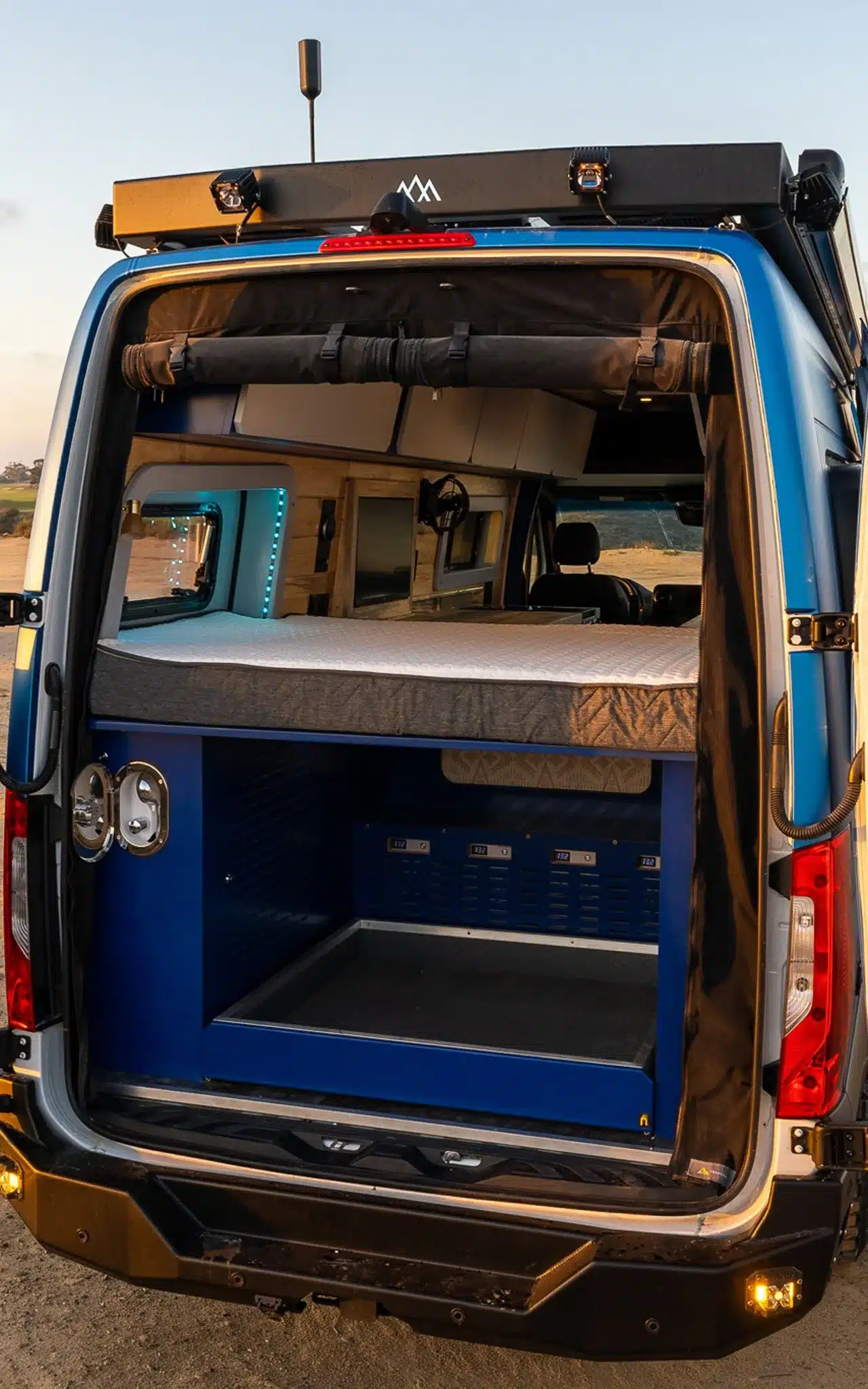 Heckansicht des Rogue Vans Fox Den mit geöffneter Tür, sichtbarem Bett und Stauraum für Technik und Gepäck