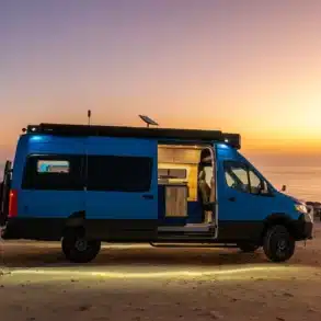 Blauer Rogue Vans Fox Den Campervan mit geöffneter Tür am Strand bei Sonnenuntergang, Innenraum sichtbar