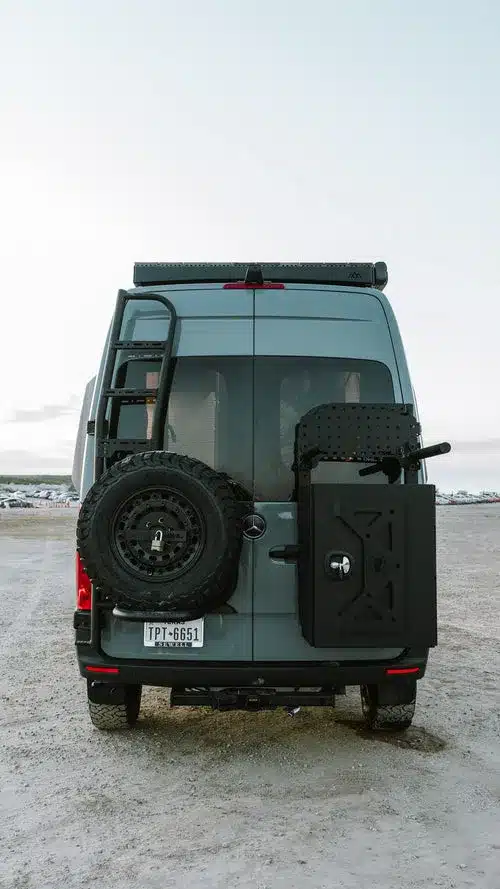 Heckansicht eines ausgebauten Kastenwagens mit Ersatzrad, Leiter und zusätzlichem Stauraum auf staubigem Untergrund