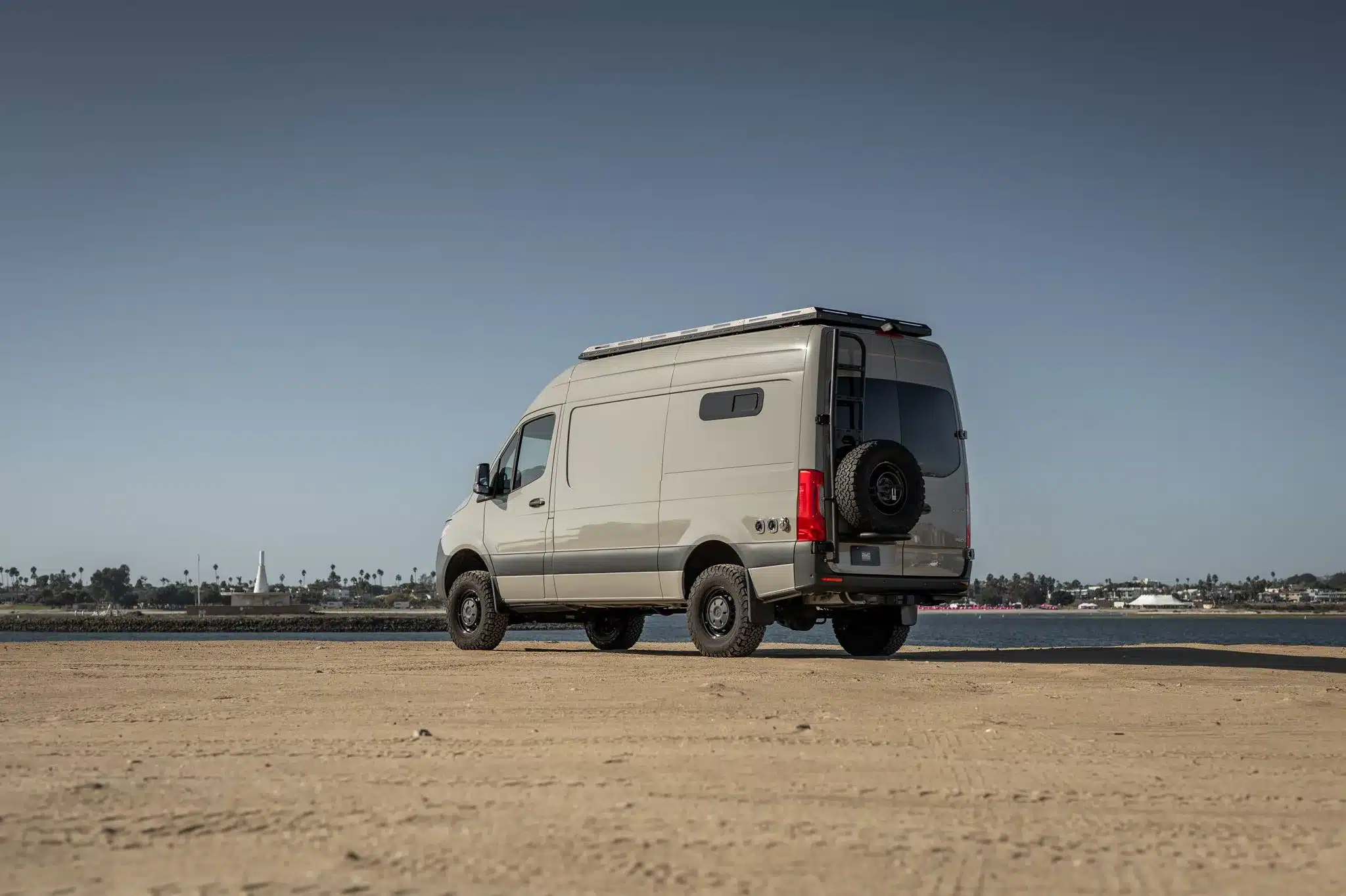 Seiten- und Heckansicht eines Rogue Vans Palisade Campervans auf sandigem Untergrund mit Blick auf das Wasser.