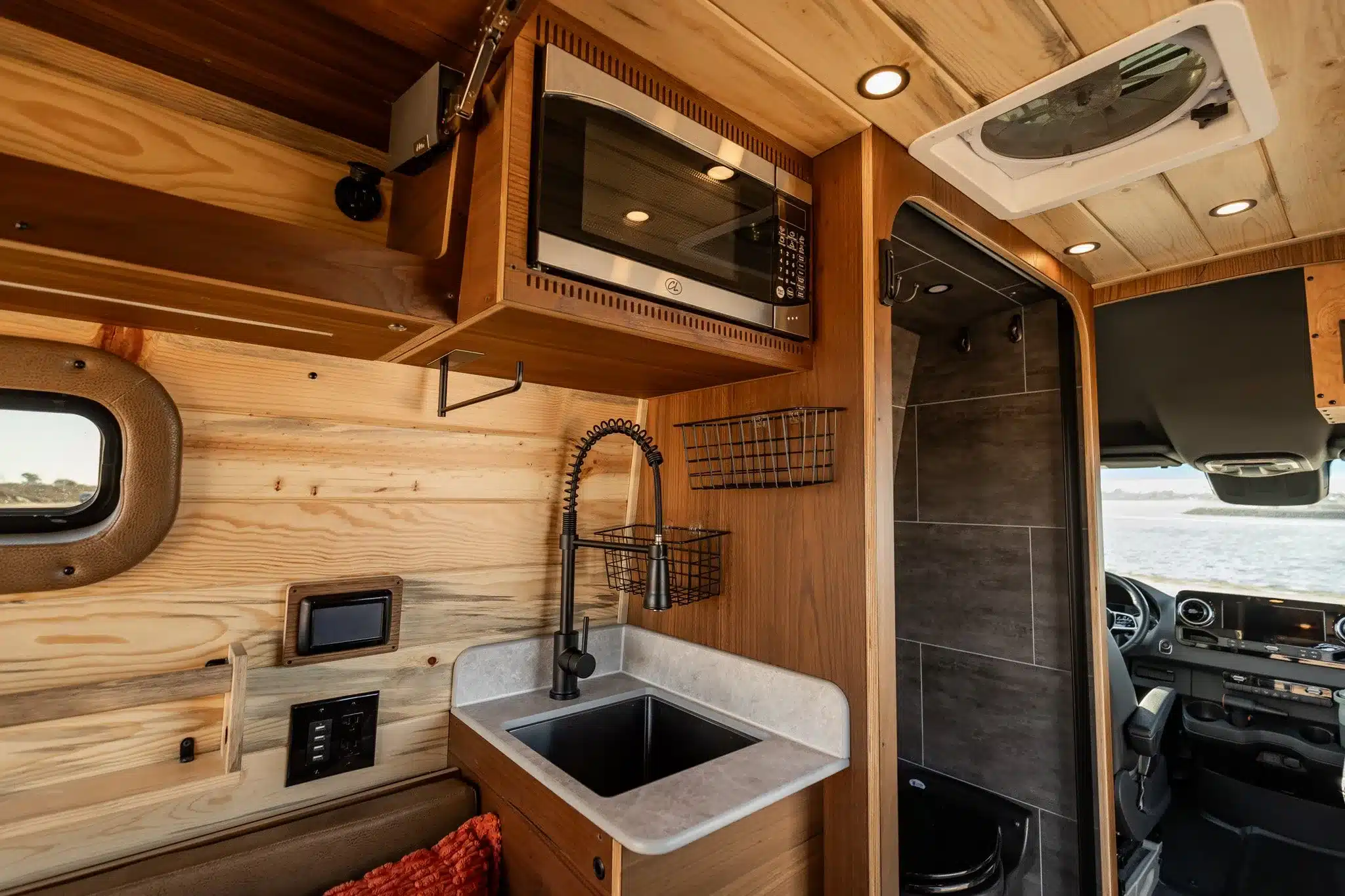 Küchenbereich mit Spüle, Mikrowelle und angrenzender Nasszelle im Rogue Vans Palisade Campervan