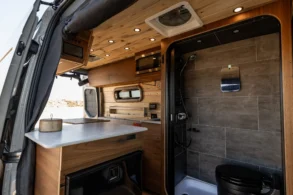Blick in den Innenraum eines Rogue Vans Palisade mit hochwertiger Nasszelle, Dusche, Toilette, Küchenzeile und Holzverkleidung