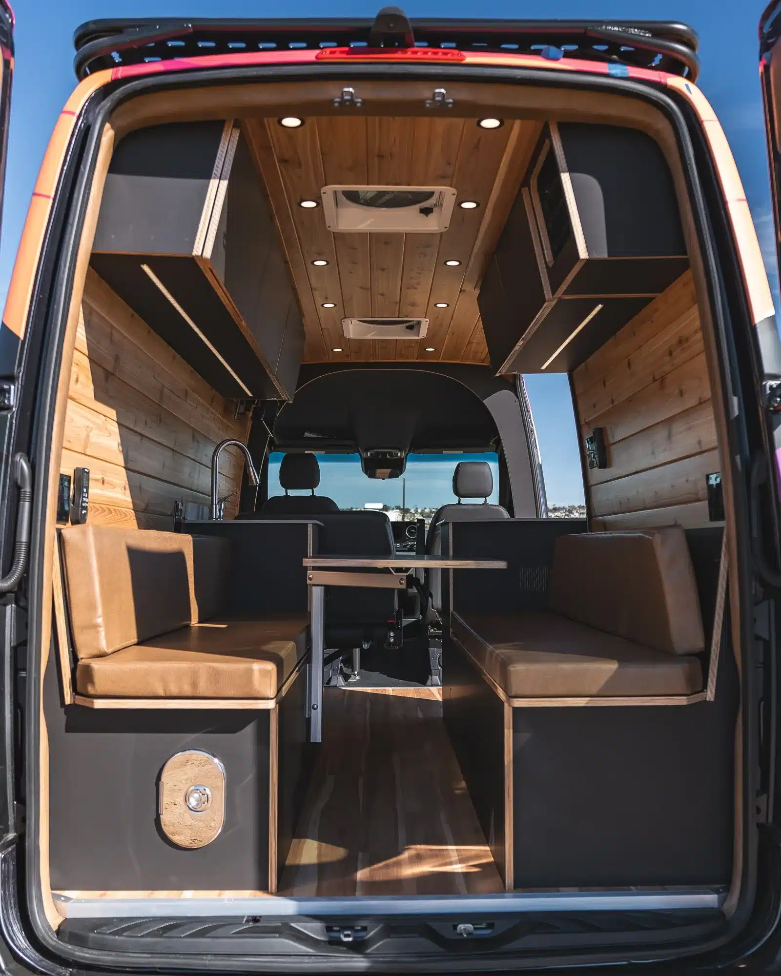 Blick in den Innenraum eines Rogue Vans Summer Classic mit zwei gepolsterten Sitzbänken, Holzausbau und moderner Beleuchtung