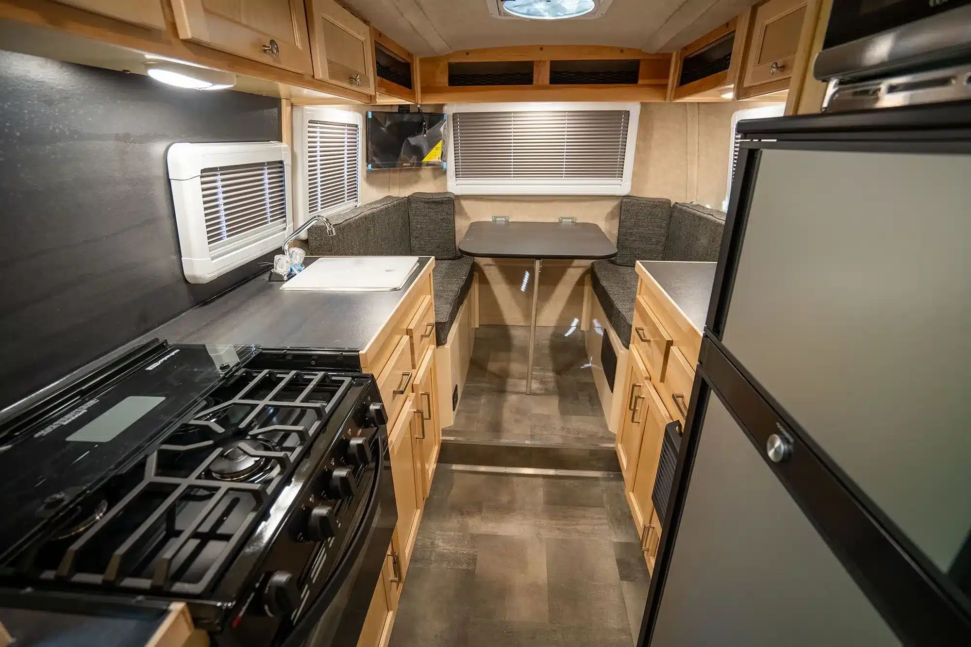 Blick in den Innenraum eines Scamp 19' Trailers mit Küchenzeile, Gasherd, Spüle, Kühlschrank und gemütlicher Sitzgruppe mit Tisch