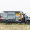 Seitenansicht eines ausgebauten Mercedes Sprinter 4x4 Campervans mit geöffneten Türen und sichtbarem Innenausbau auf einer Wiese