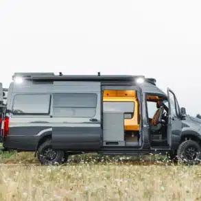 Seitenansicht eines ausgebauten Mercedes Sprinter 4x4 Campervans mit geöffneten Türen und sichtbarem Innenausbau auf einer Wiese