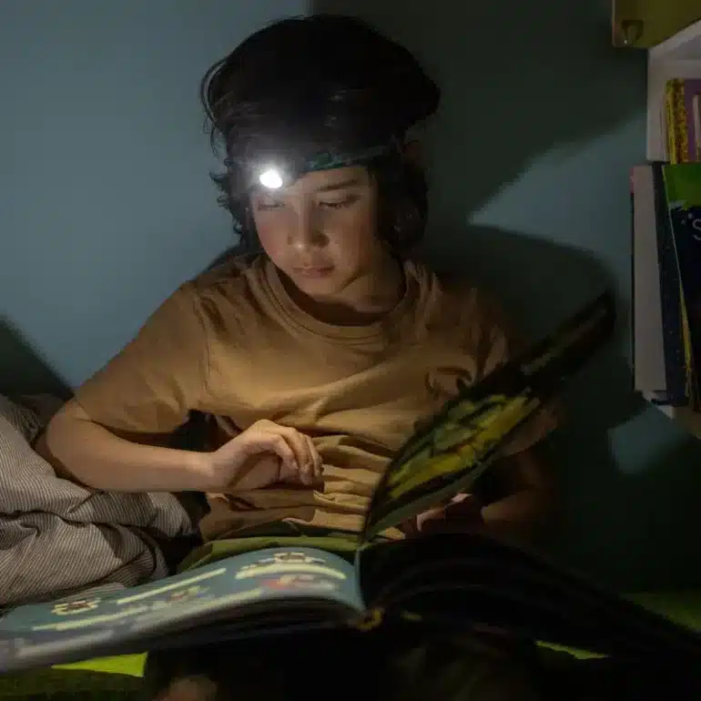 Kind mit KIDLED4R Stirnlampe liest ein Buch im Dunkeln im Camper.