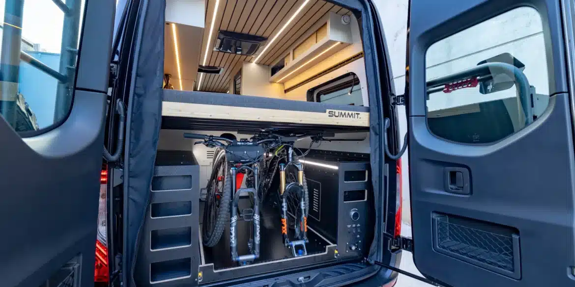 Heckansicht des SUMMIT L1 Vans mit geöffneter Tür, großem Stauraum und zwei Mountainbikes unter dem erhöhten Bett