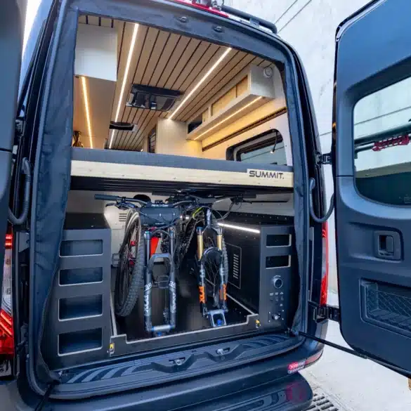 Heckansicht des SUMMIT L1 Vans mit geöffneter Tür, großem Stauraum und zwei Mountainbikes unter dem erhöhten Bett